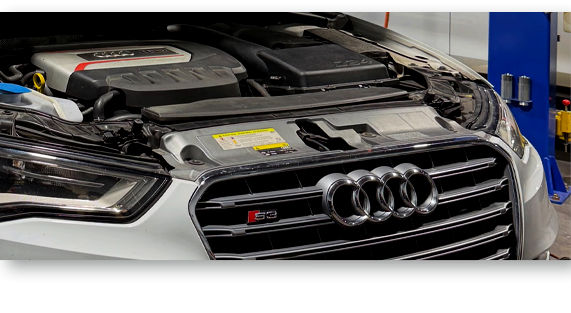 Audi sedan with hood open in a garage, showing the front grille and engine bay