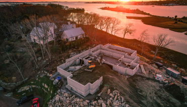 An aerial view of a house under construction next to a body of water at sunset.