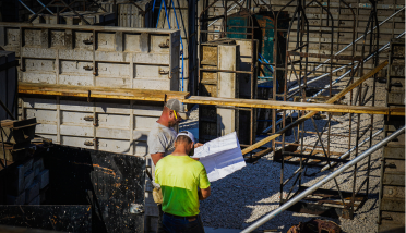 Two construction workers are looking at a blueprint at a construction site.