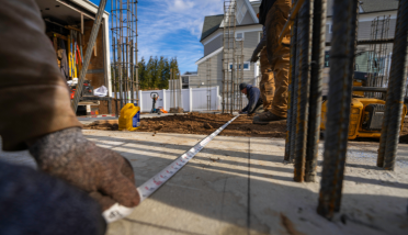 A construction worker is measuring a building with a tape measure.