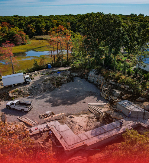 An aerial view of a construction site surrounded by trees and a body of water.