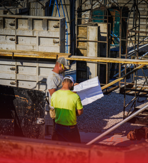 Two construction workers are looking at a blueprint on a construction site.