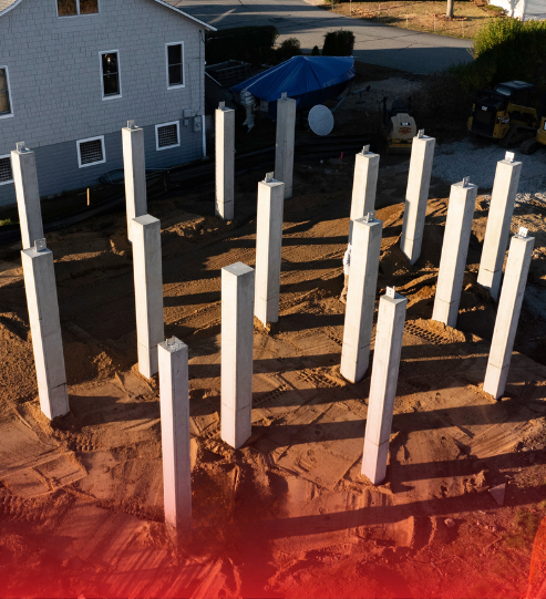 A bunch of concrete pillars are in the dirt in front of a house