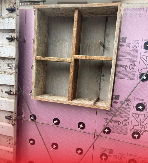 A wooden shelf is attached to a wall with pink styrofoam.