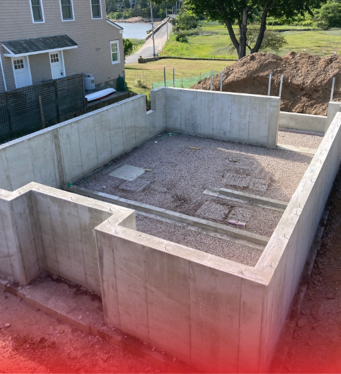 A concrete basement under construction with a house in the background.