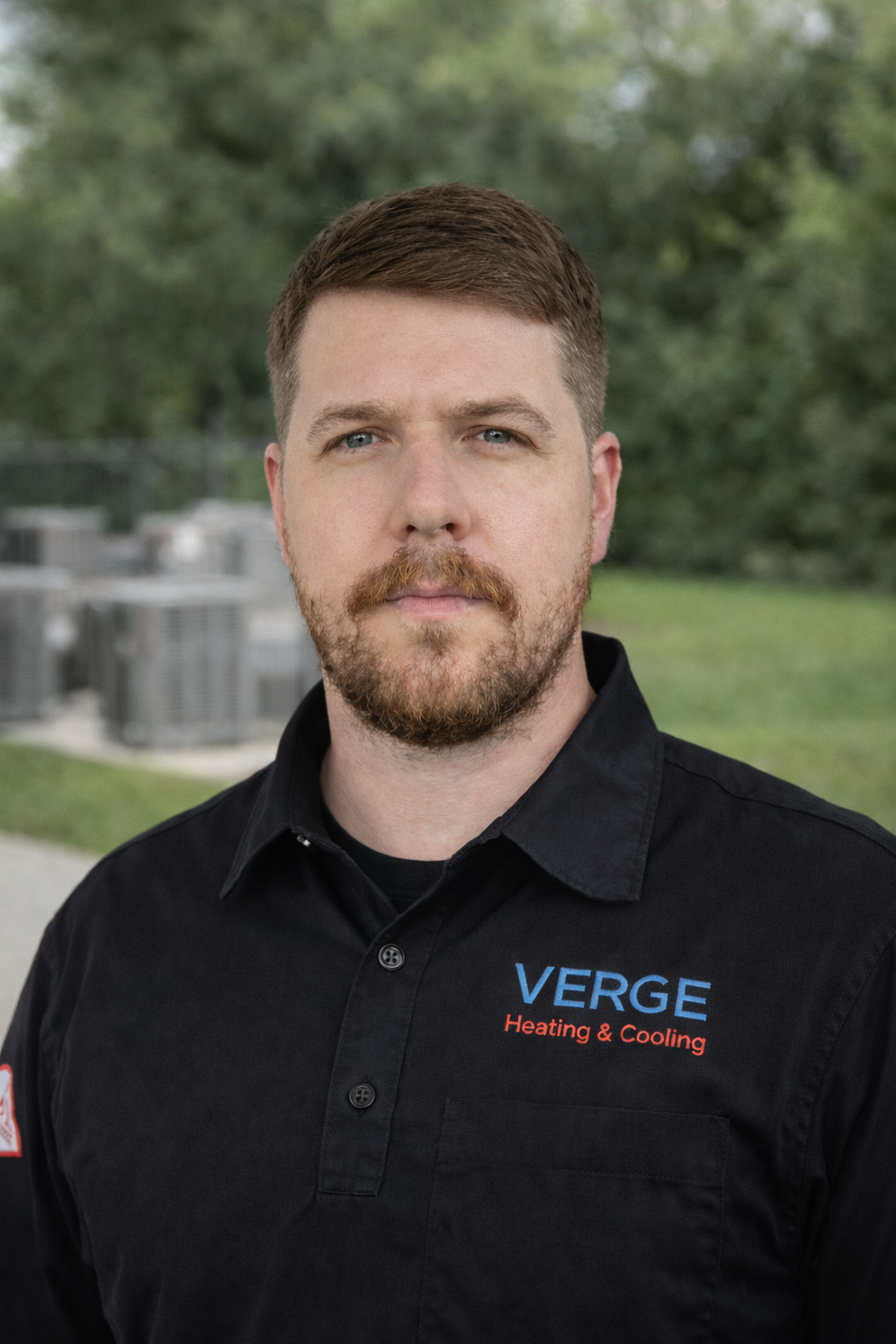 Man in black Verge Heating & Cooling shirt standing outdoors with a neutral expression