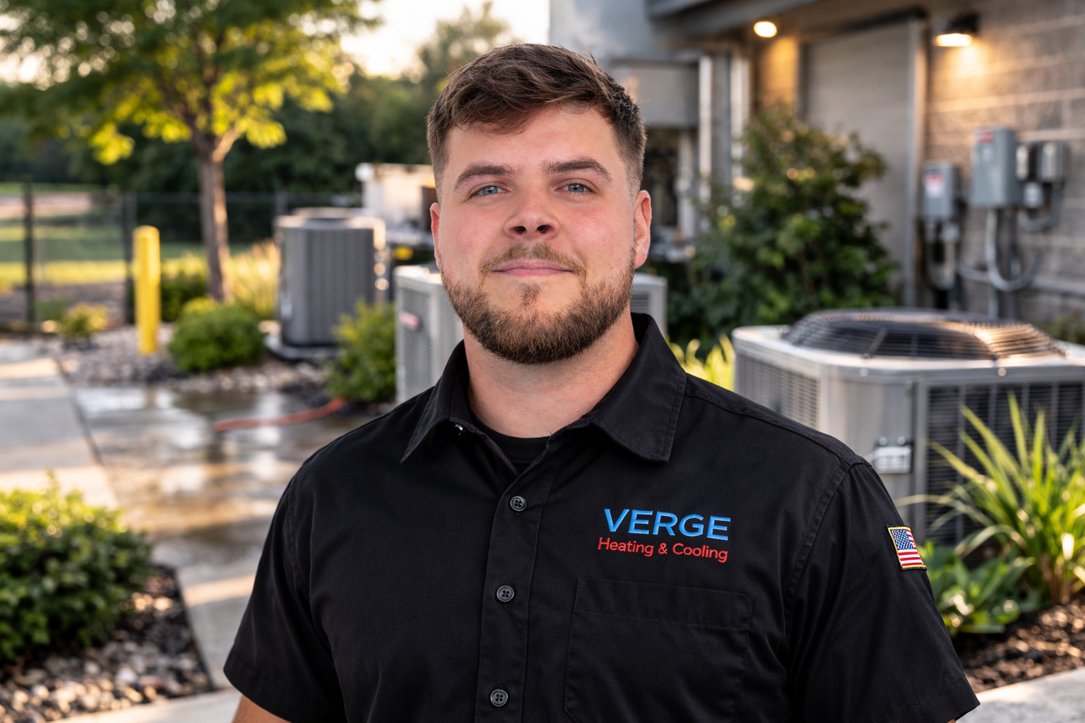 Man in black Verge shirt standing outdoors in a landscaped residential area at dusk.