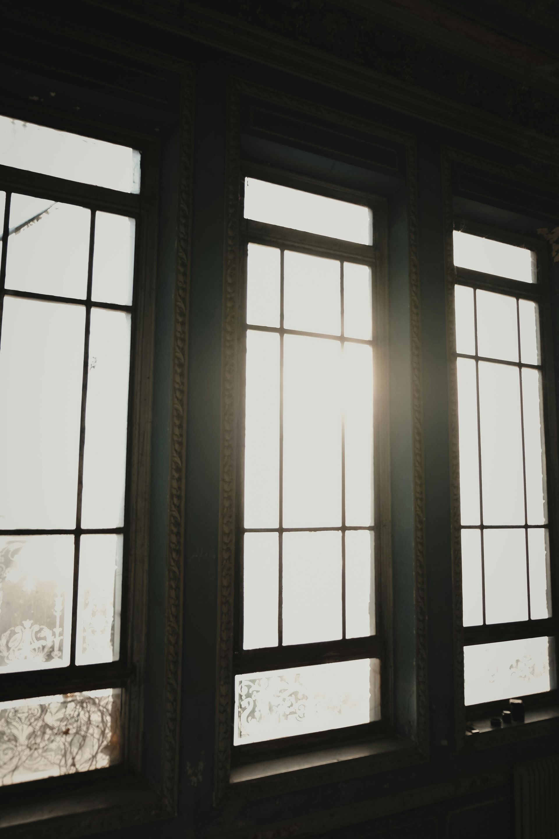 Sunlight streaming through three tall window panes in a dim room