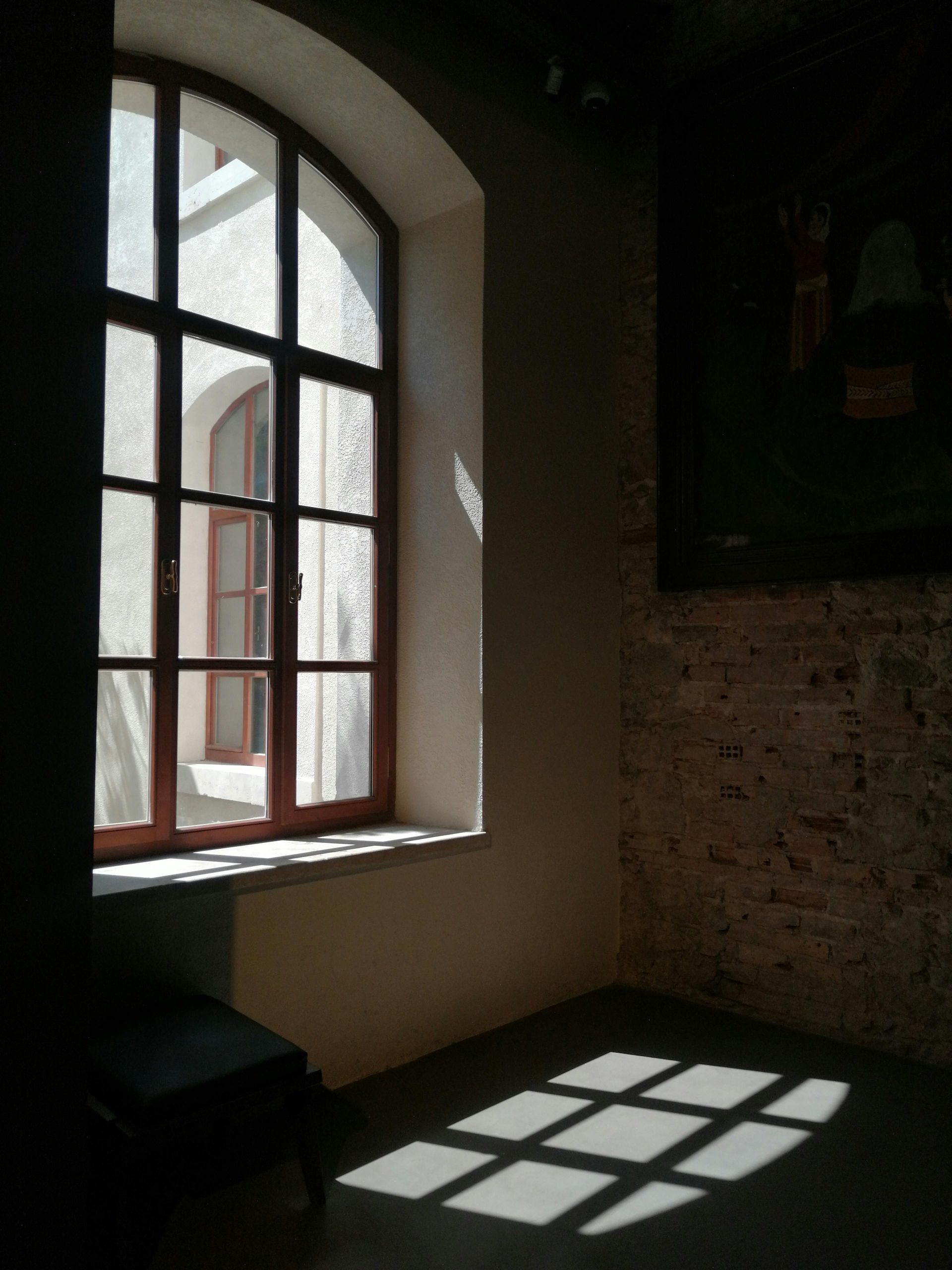Sunlit room with an arched window casting a grid of shadows on the floor and wall