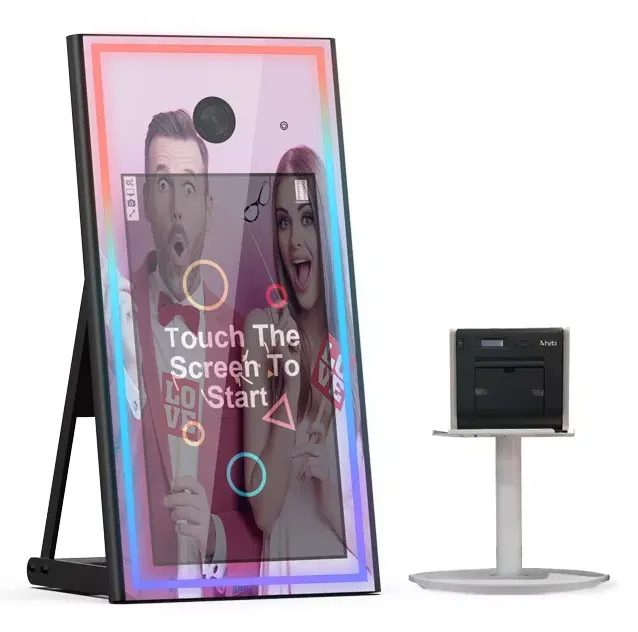 Photo booth mirror with colorful frame, displaying two people, and a printer on a stand.