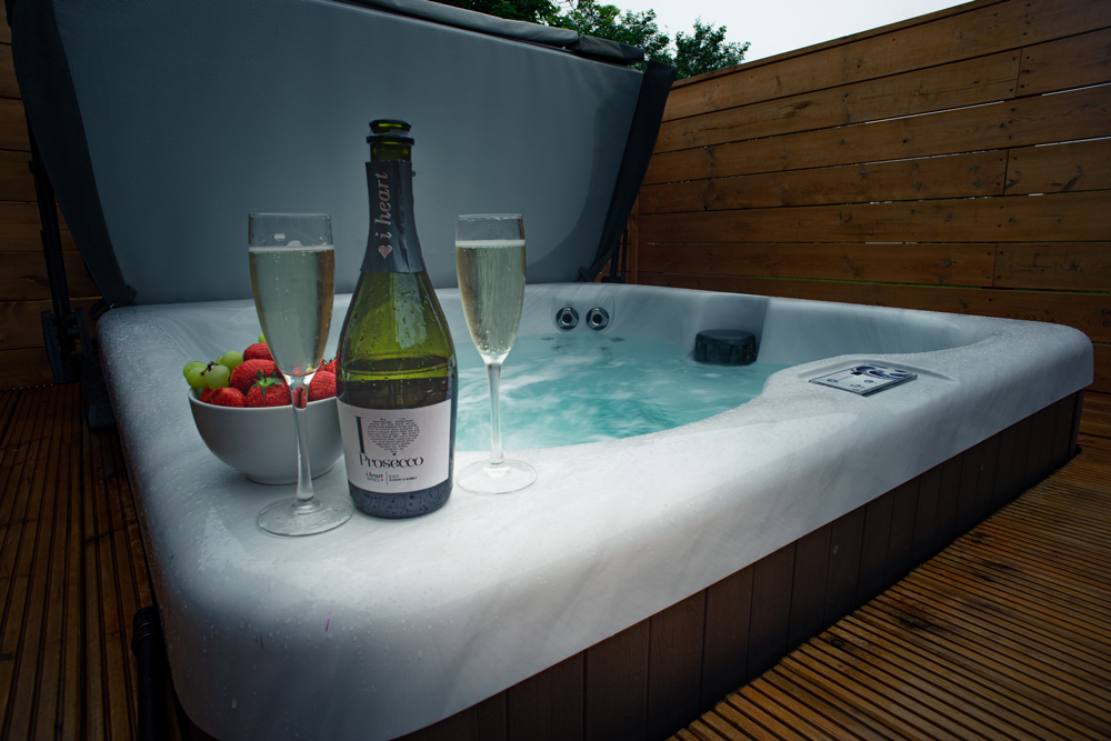 Hot tub with champagne, glasses, and fruit on a wooden deck.