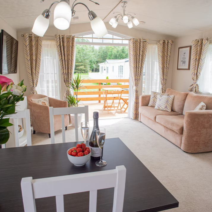 Cozy living room with sliding doors opening onto a deck. Features sofa, chairs, dining table with champagne, and a view.