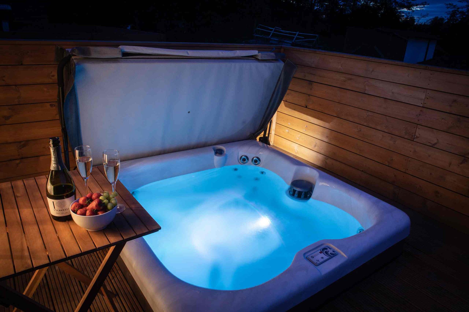 hot tub turned with bubbles and lights, bottle of wine and strawberries near hot tub