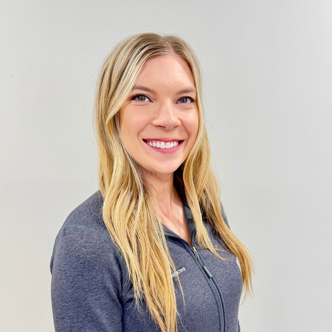 Smiling blonde woman in a gray top against a plain light background