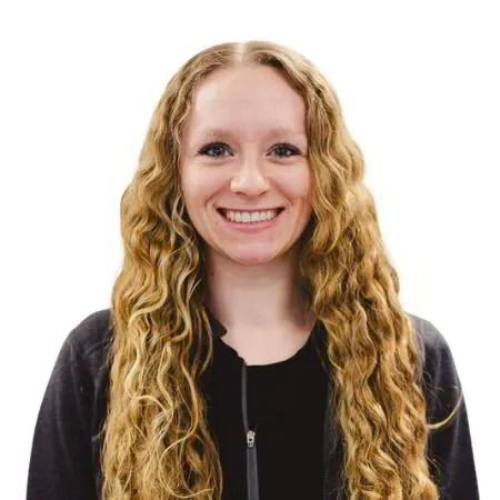 Smiling person with long wavy blonde hair wearing a black jacket against a white background