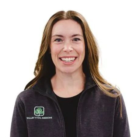 Smiling person in a black jacket with a Vital Medicine logo on a white background