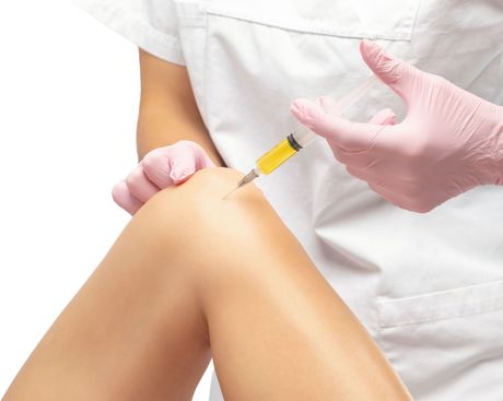 Healthcare worker injecting a syringe into a bent knee during a medical procedure