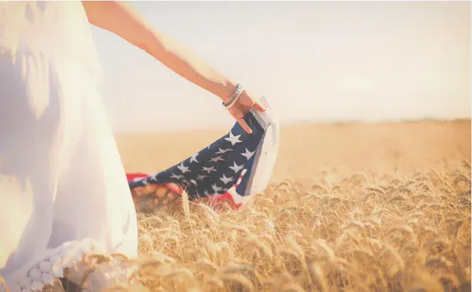 Hand holding an American flag in a sunlit wheat field