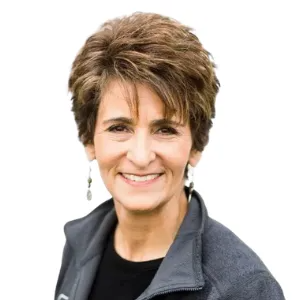 Smiling woman with short brown hair wearing a gray jacket on a white background
