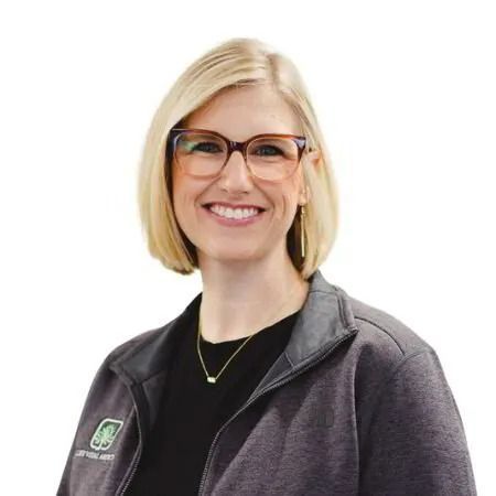 Smiling blonde woman wearing glasses and a dark zip-up jacket on a white background