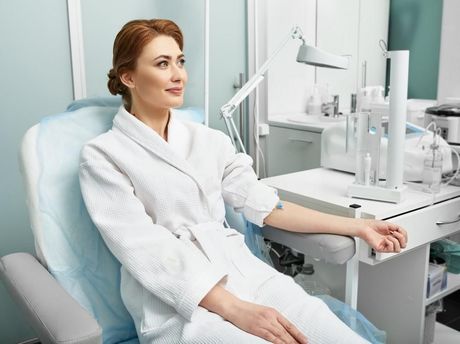 Woman in a dental chair, wearing a white robe, at a bright modern clinic with dental equipment nearby