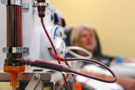 IV tubing and medical equipment in foreground, with a patient blurred in a hospital bed behind it