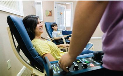 Person receiving a hand massage in a spa chair while a therapist adjusts controls nearby