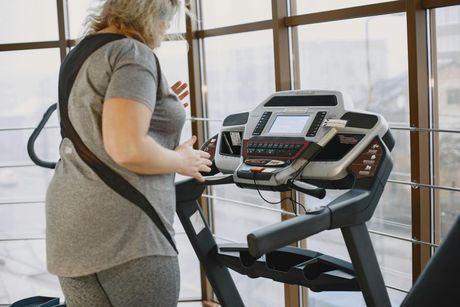 Person walking on a treadmill in a bright gym, seen from behind.