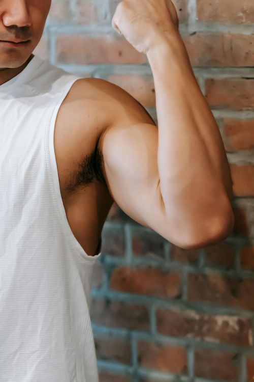 Arm flexed in a white tank top against a brick wall