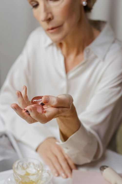 Woman holding a small pink pill above a table with a glass of water and medication bottles