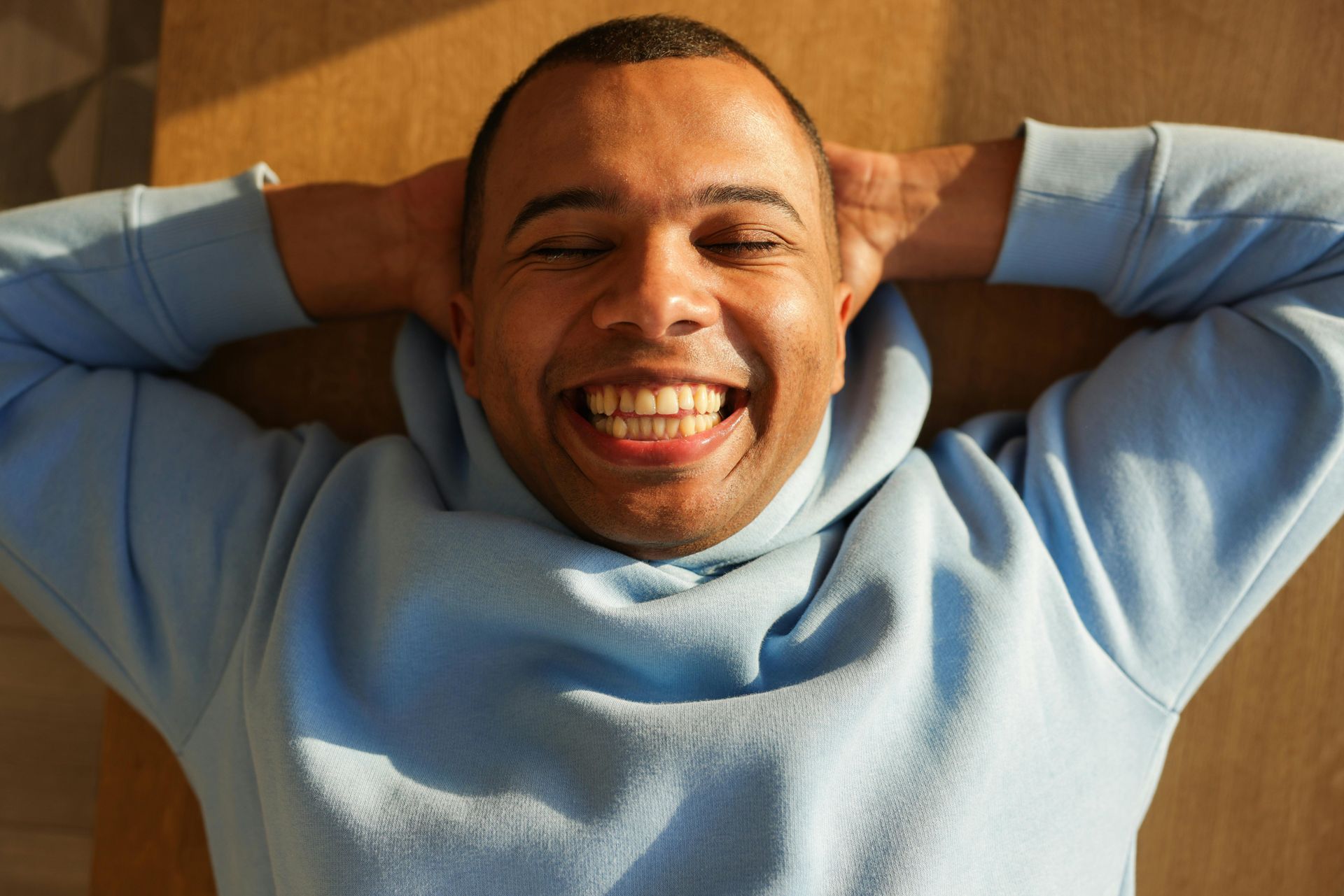 Smiling person in a light blue sweater lounging with hands behind head on a couch