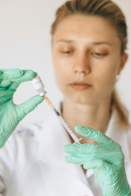 Gloved hands drawing liquid into a syringe while a lab worker watches in a clinical setting