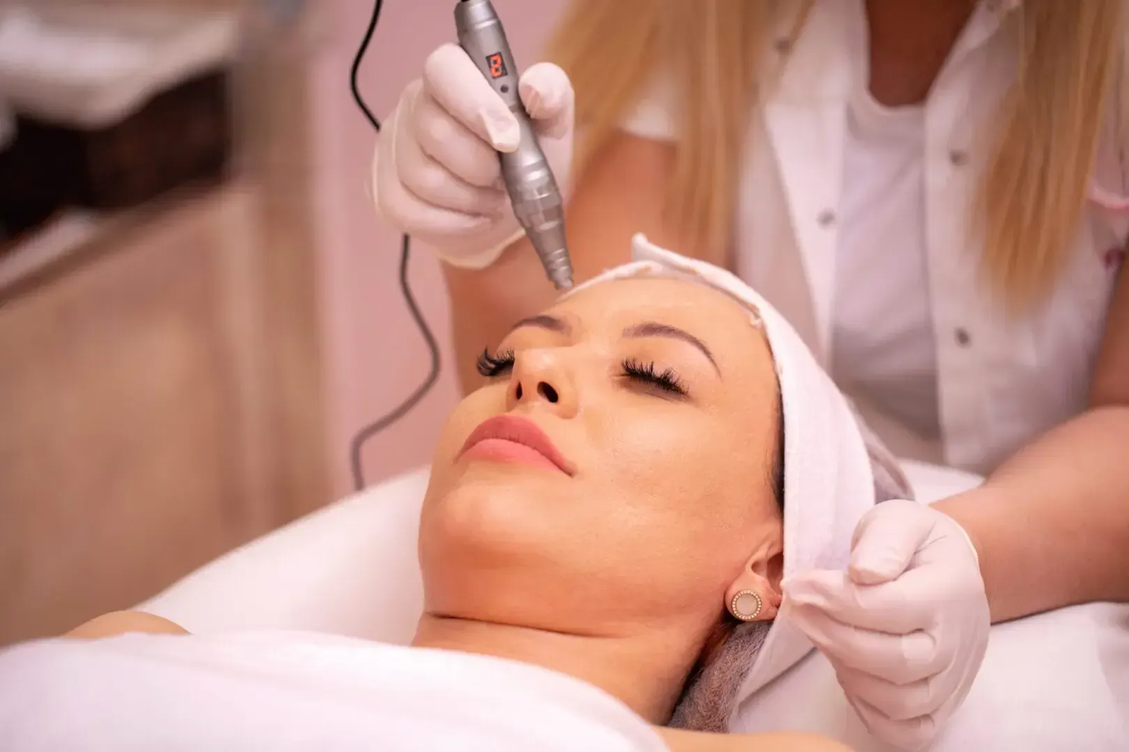 Cosmetic treatment on a woman’s forehead with a handheld device in a spa setting
