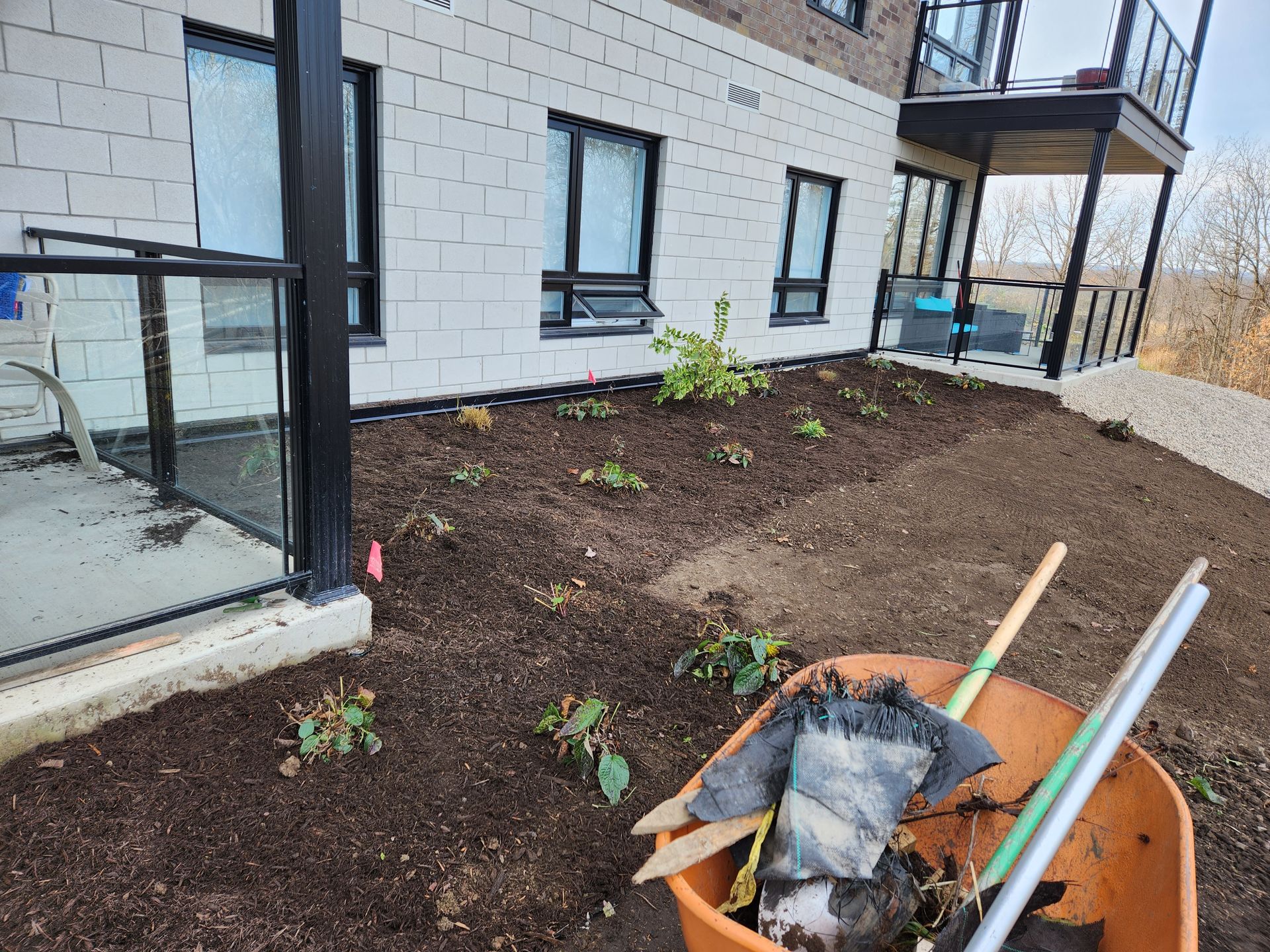 Nouvelle terrasse d'appartement avec du paillis frais, des petites plantes et des outils de jardinage près d'une porte vitrée