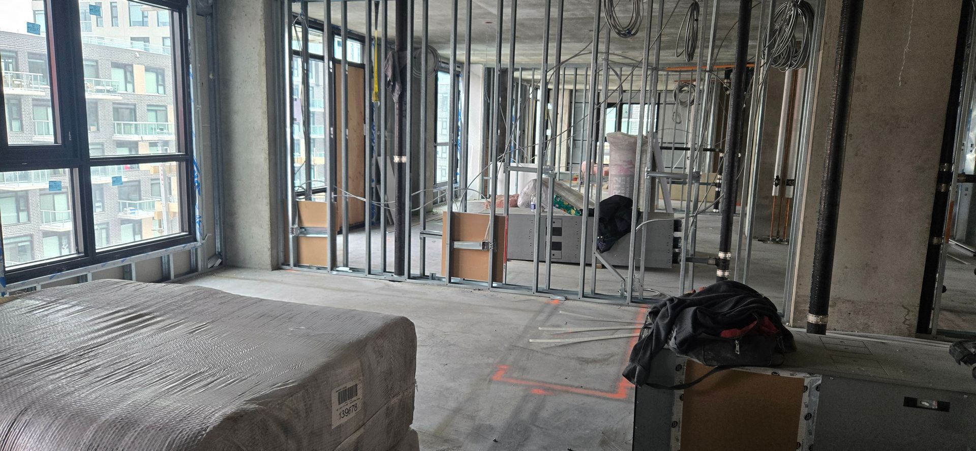 Intérieur d'appartement inachevé avec charpente apparente, fenêtres et matériaux de construction.