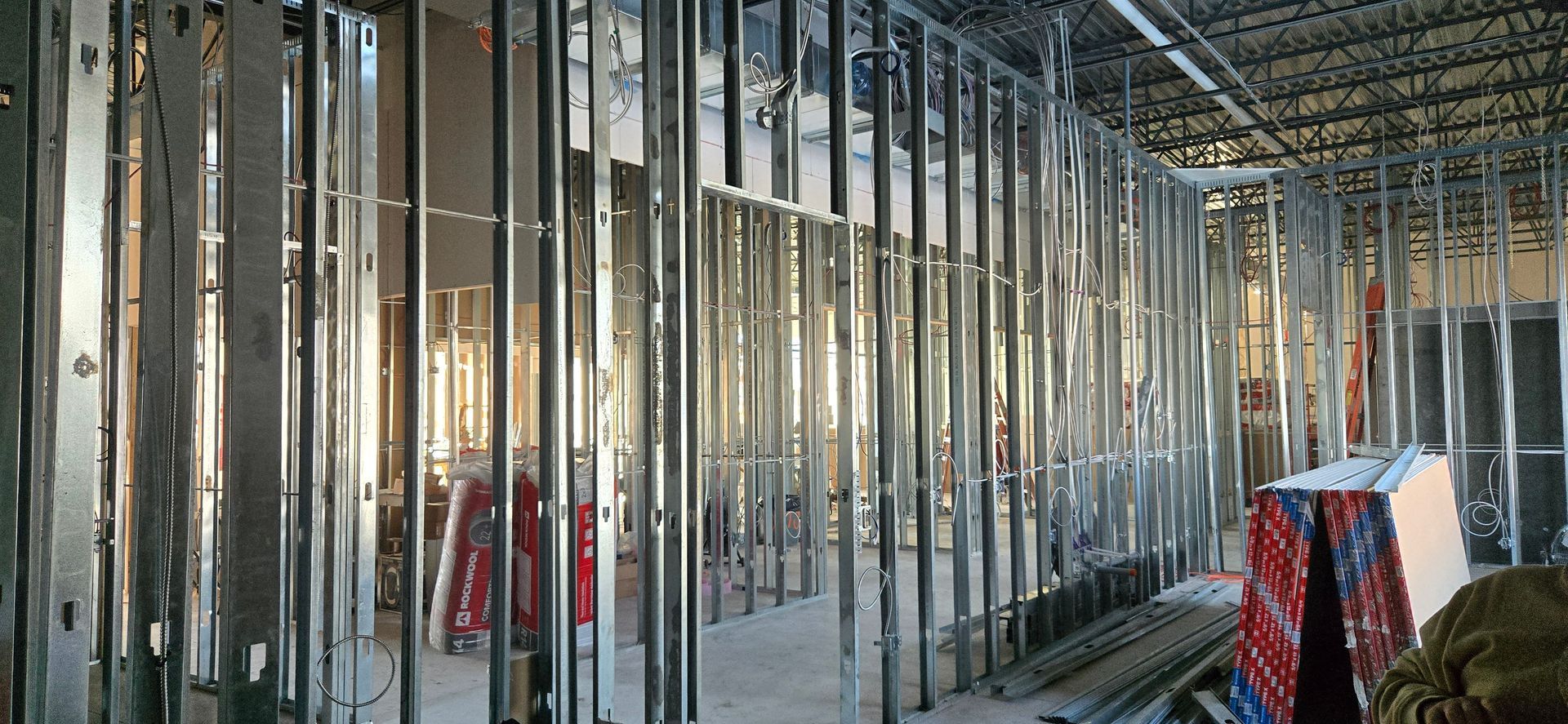 Intérieur d'un bâtiment en construction avec des montants métalliques apparents et des plaques d'isolation suspendues.