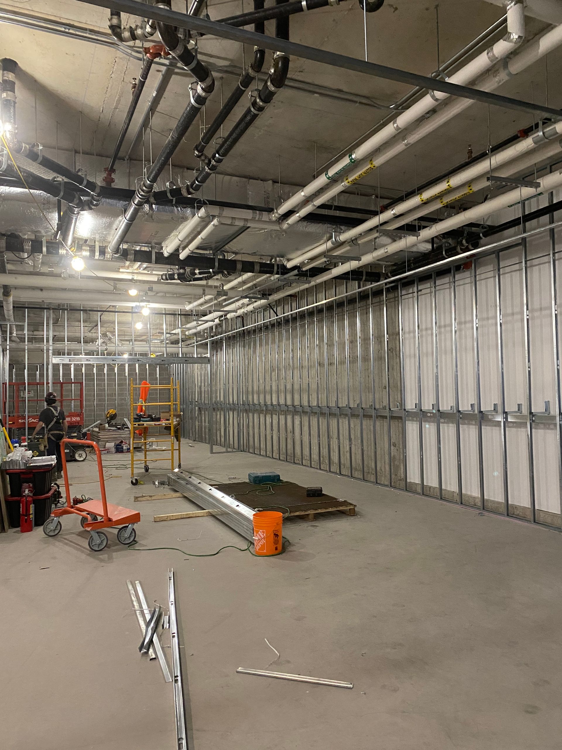 Intérieur d'un chantier de construction avec conduits de plafond apparents, panneaux muraux blancs, outils et ouvriers sur un sol en béton