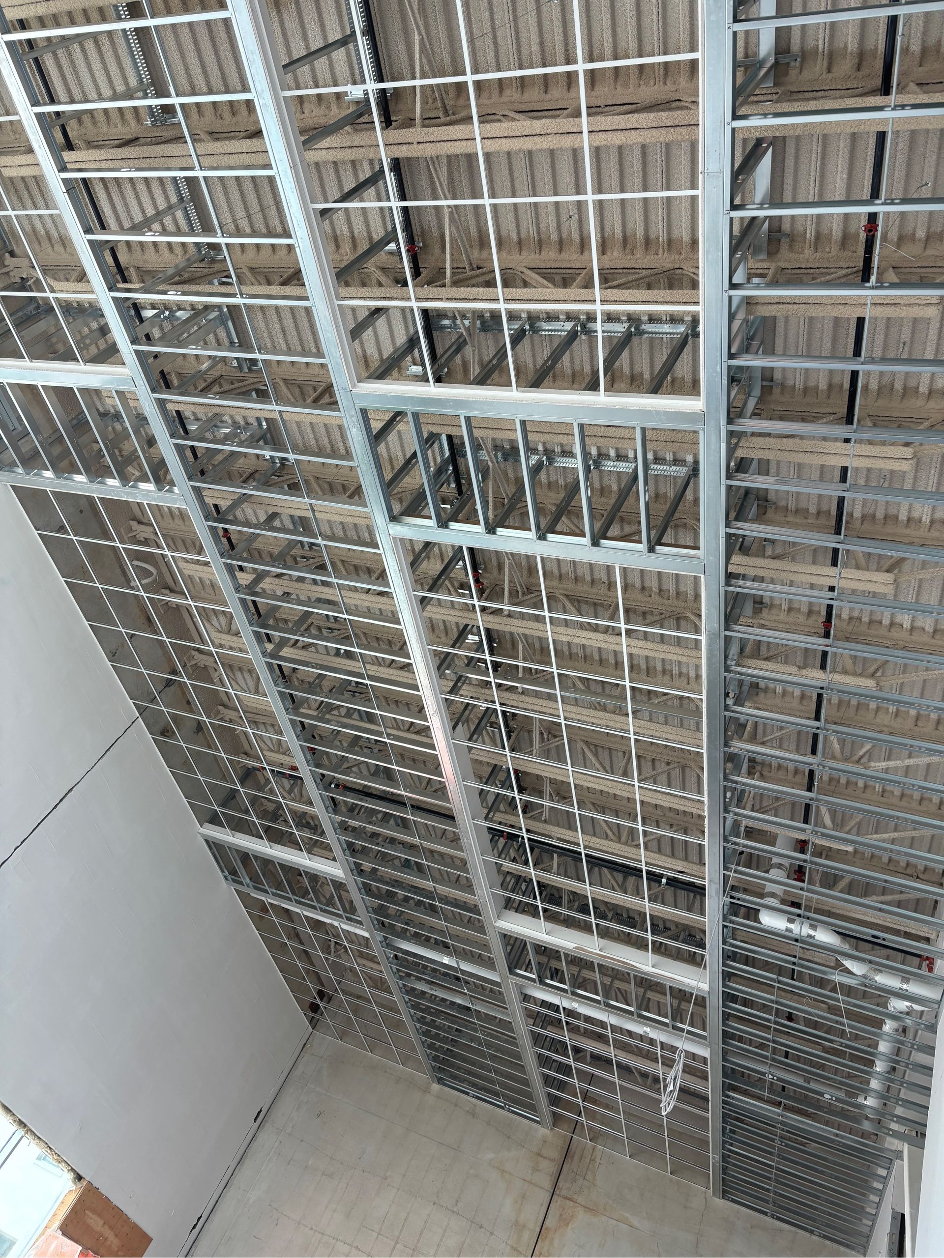 Vue intérieure d'un haut mur en grille métallique avec des étagères, vue d'en bas dans un espace étroit aux murs blancs.