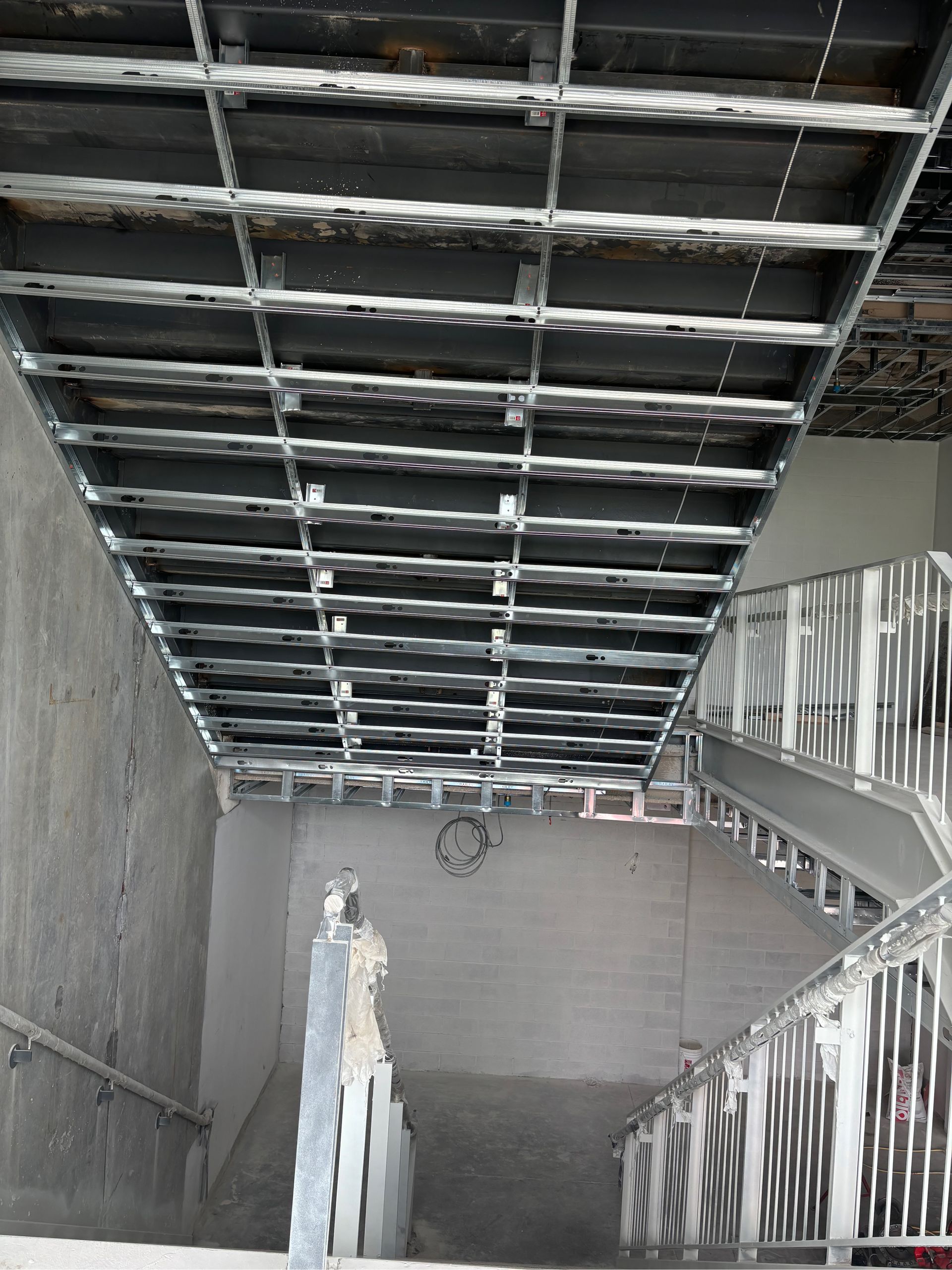 Escalier souterrain en construction, avec charpente de plafond apparente et rampes blanches.