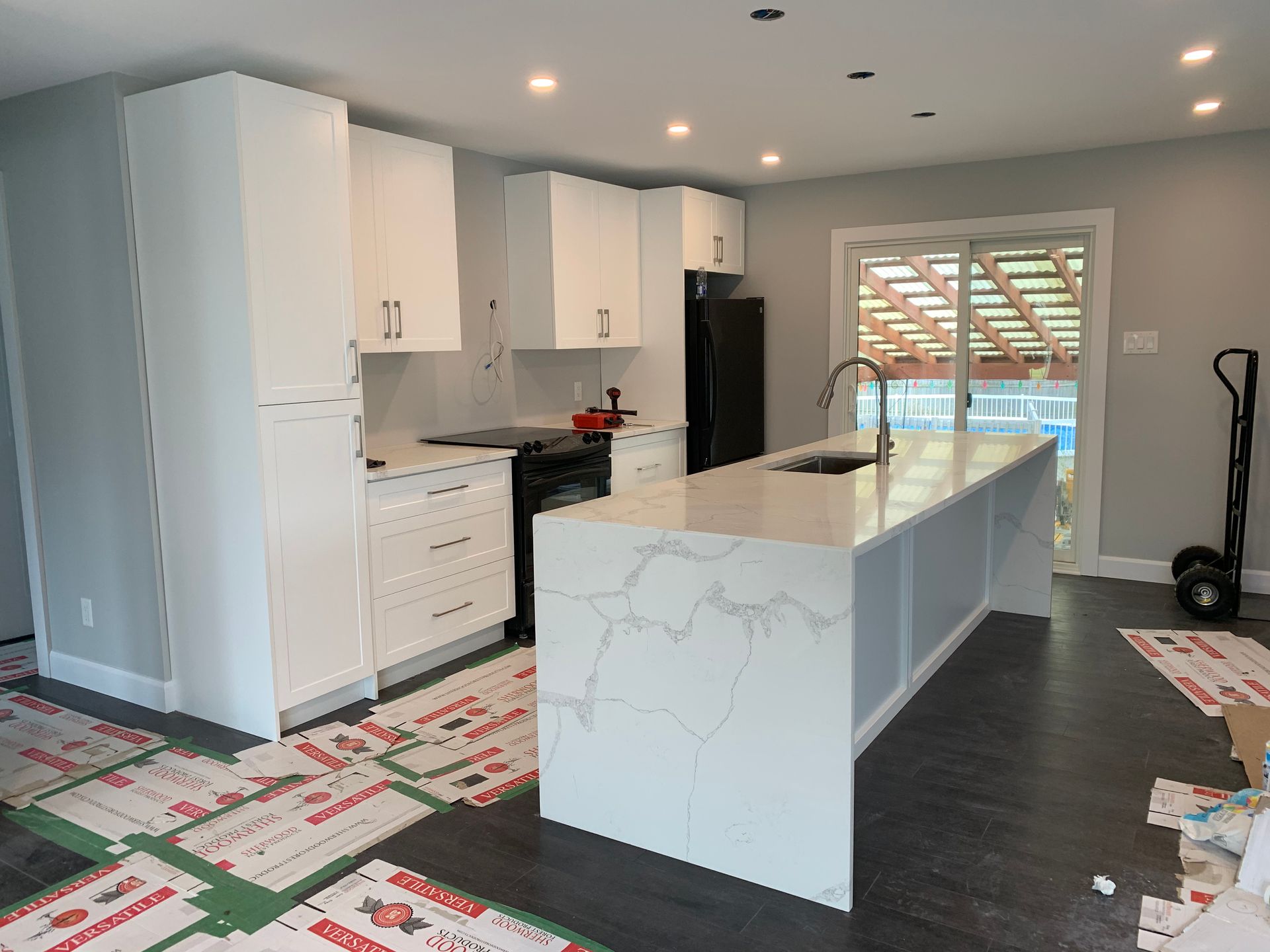 Cuisine blanche moderne en cours de rénovation avec îlot central, placards, comptoirs en granit et revêtements de sol protecteurs.
