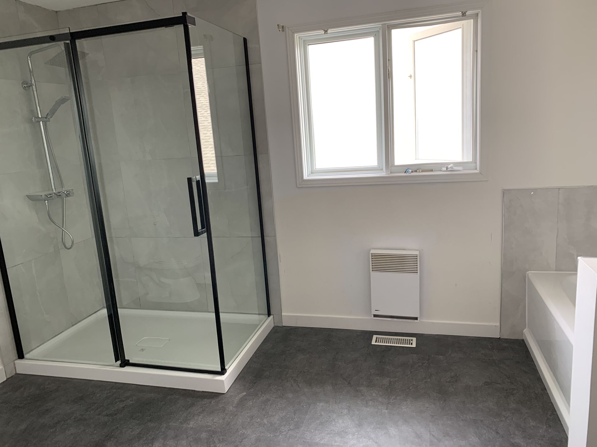 Salle de bains moderne avec douche en verre, fenêtre, toilettes et moquette grise au sol