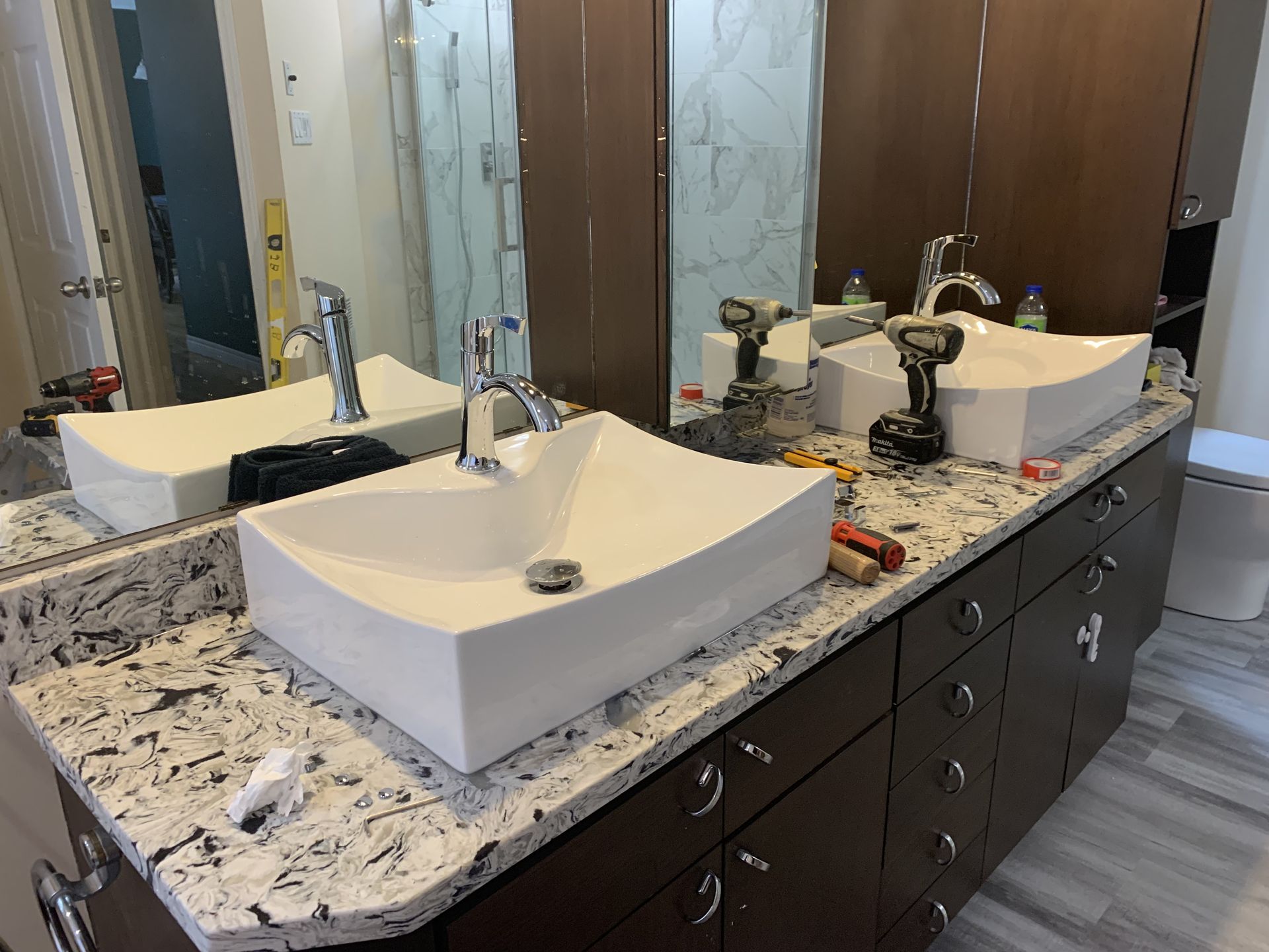 Meuble-lavabo moderne avec deux vasques blanches, comptoir en granit et armoires en bois foncé.