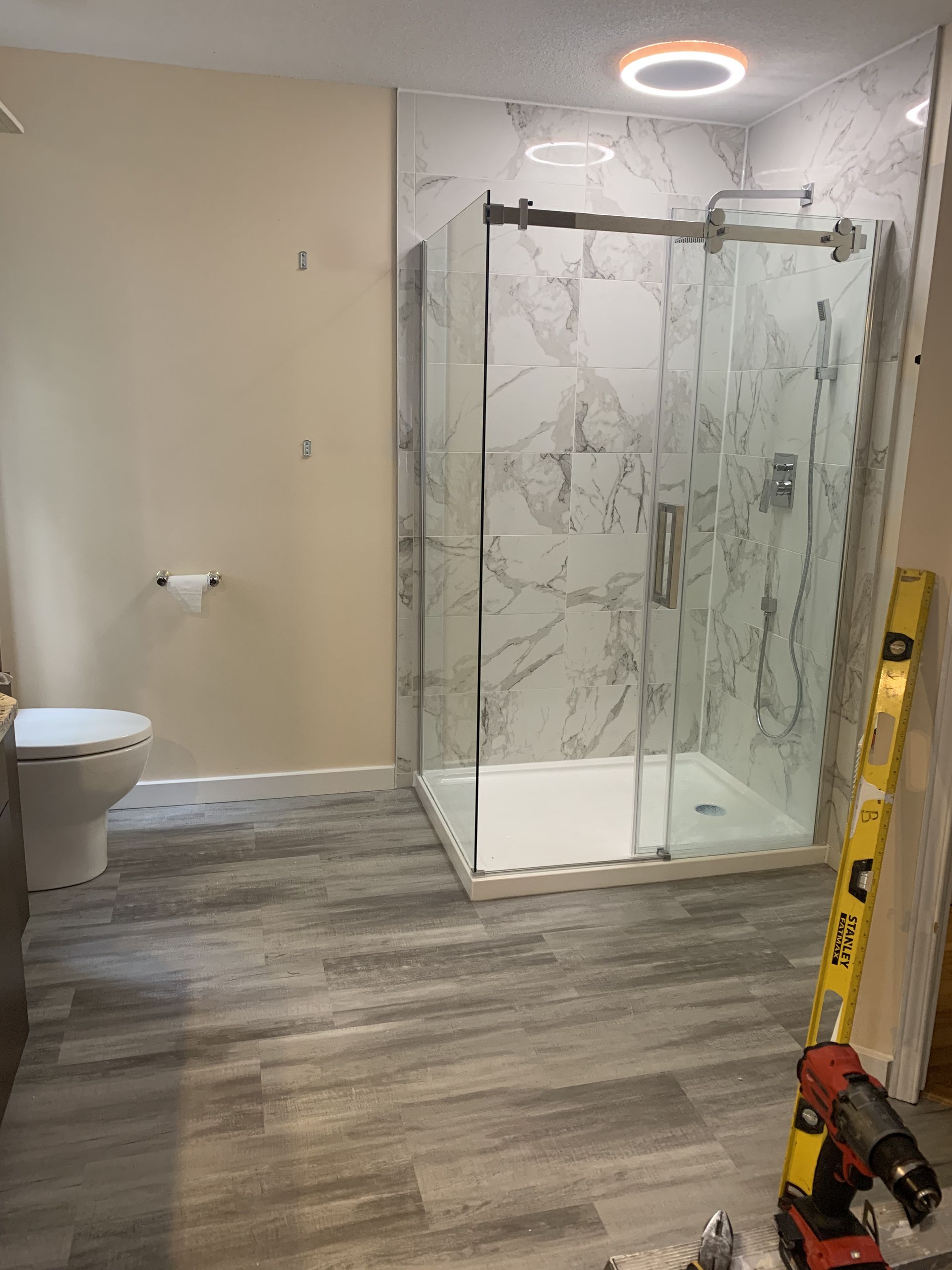 Salle de bains moderne avec douche en verre, toilettes, sol imitation bois gris et murs beiges