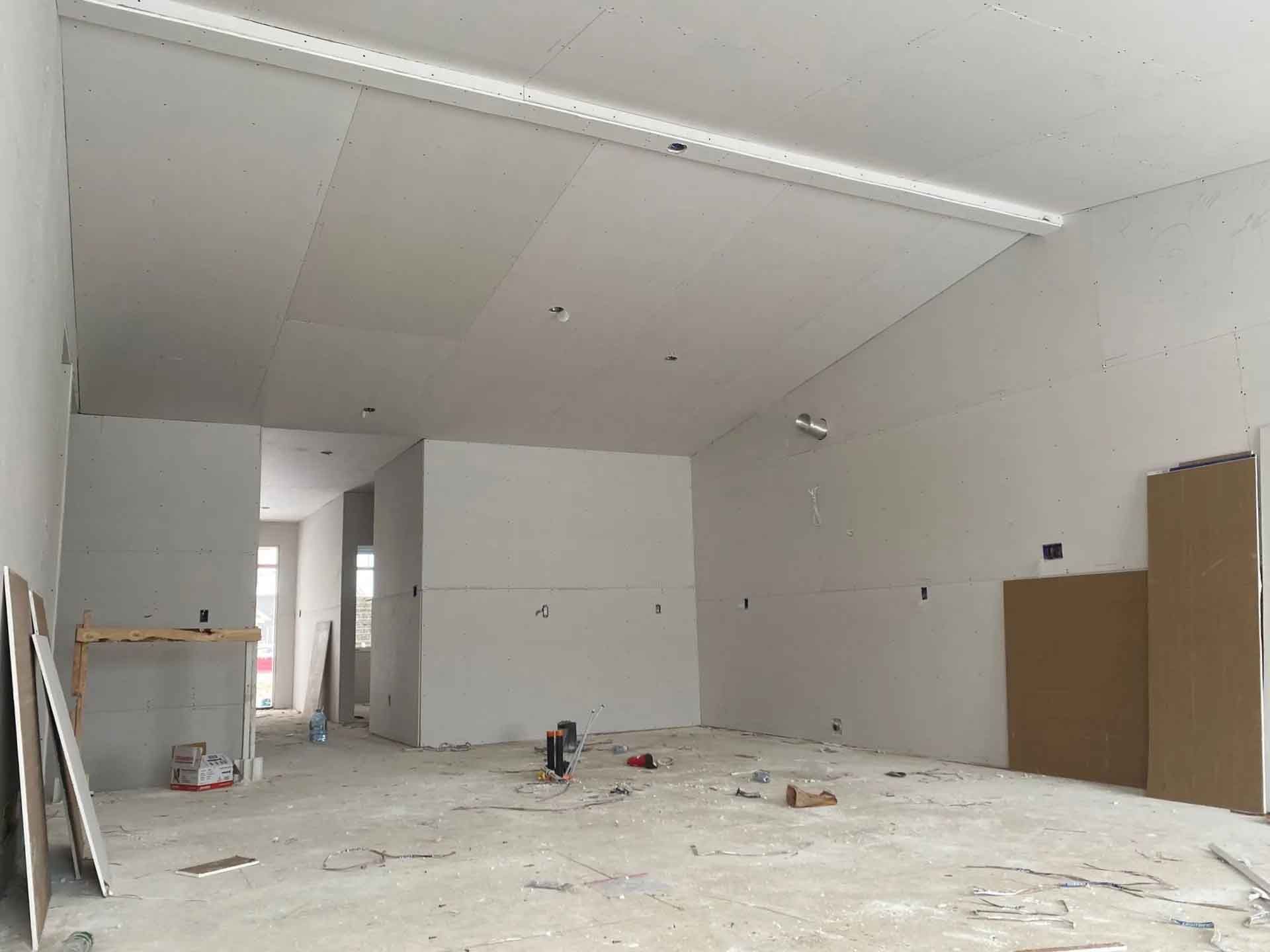Pièce vide et inachevée avec cloisons sèches blanches, sol apparent et matériaux de construction.