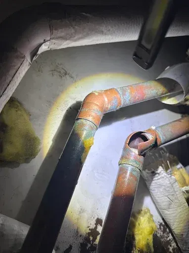 Flashlight illuminating rusty pipes and insulated ducts in a dark utility space