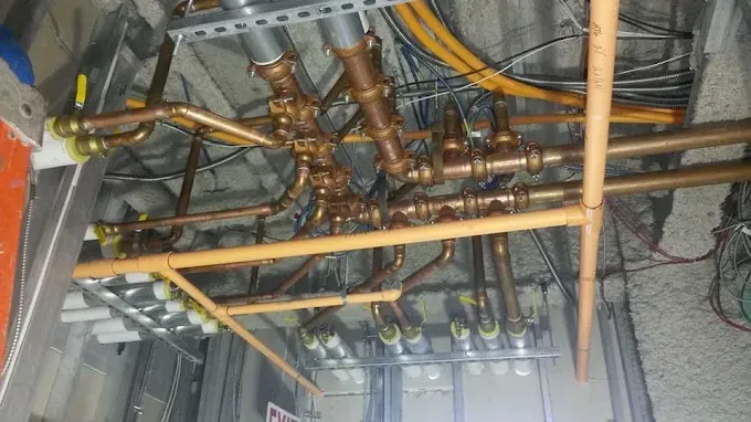Overhead view of copper pipes and cables in an industrial ceiling space