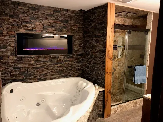 Bathroom with a white soaking tub, stone accent wall, and glass-enclosed shower.