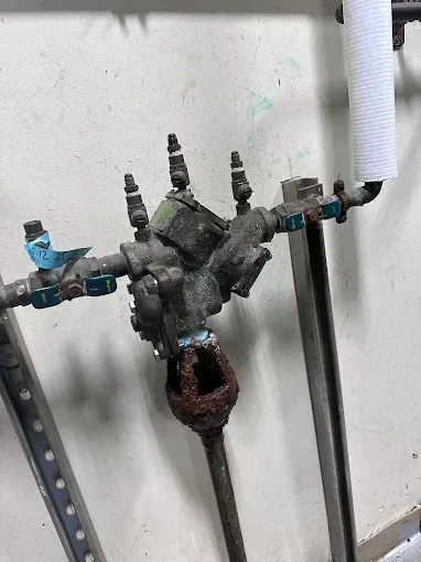 Old rusty plumbing valve and pipes mounted on a white wall.