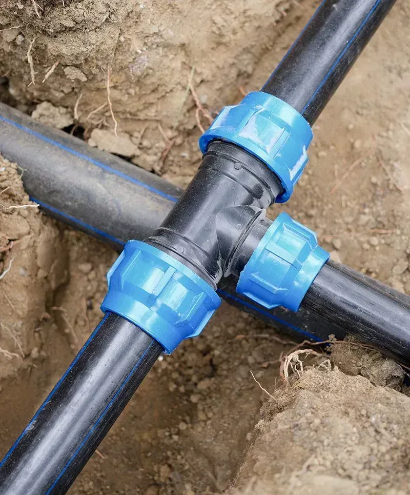 Blue irrigation pipe connector joining three black pipes in dirt