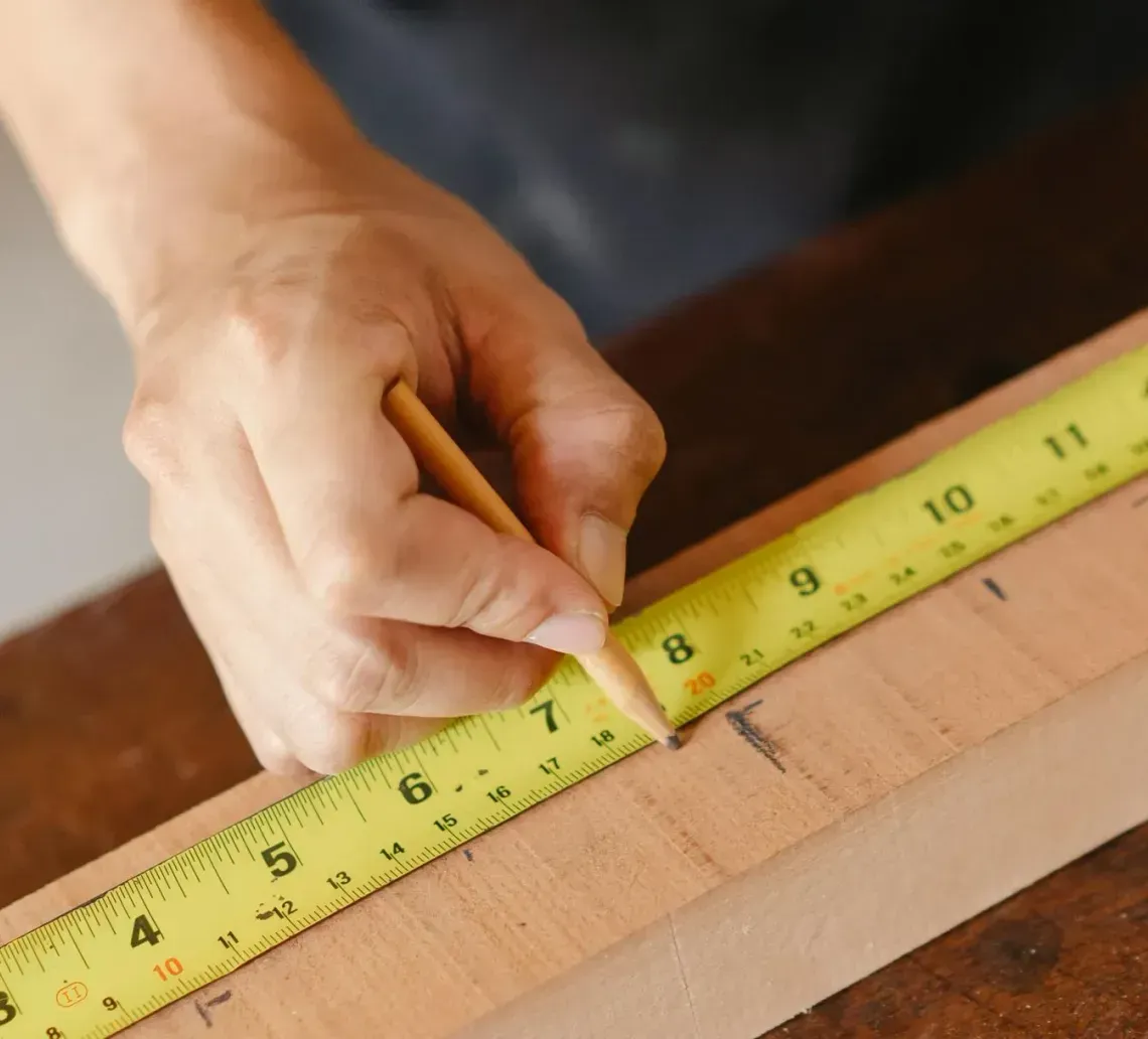 Hand marking measurement on wood with a pencil and measuring tape.